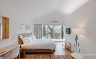 Bedroom with bed with white linen on wooden floor and door leading to balcony with stunning view