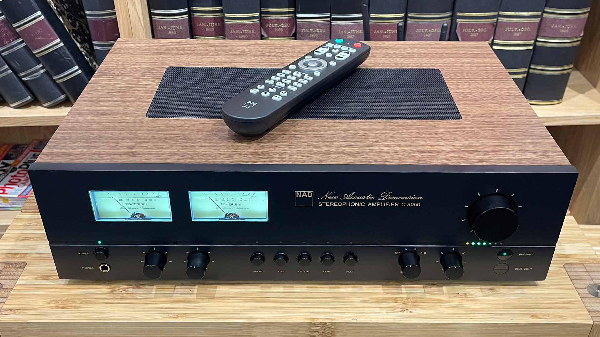 NAD C 3050 (with MDC2 BluOS-D module) streaming amplifier on wooden hi-fi rack in front of bookcase with remote sitting on top