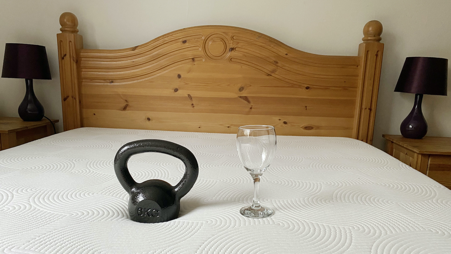 A 6kg black weight is dropped near an empty wine glass on the Brook + Wilde Lux Mattress during the review process to test motion isolation