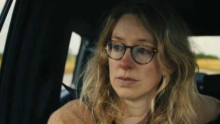 A close up of Elizabeth Holmes in a car, wearing tortoise shell glasses as she heads to report to prison in You Can See Everything. 