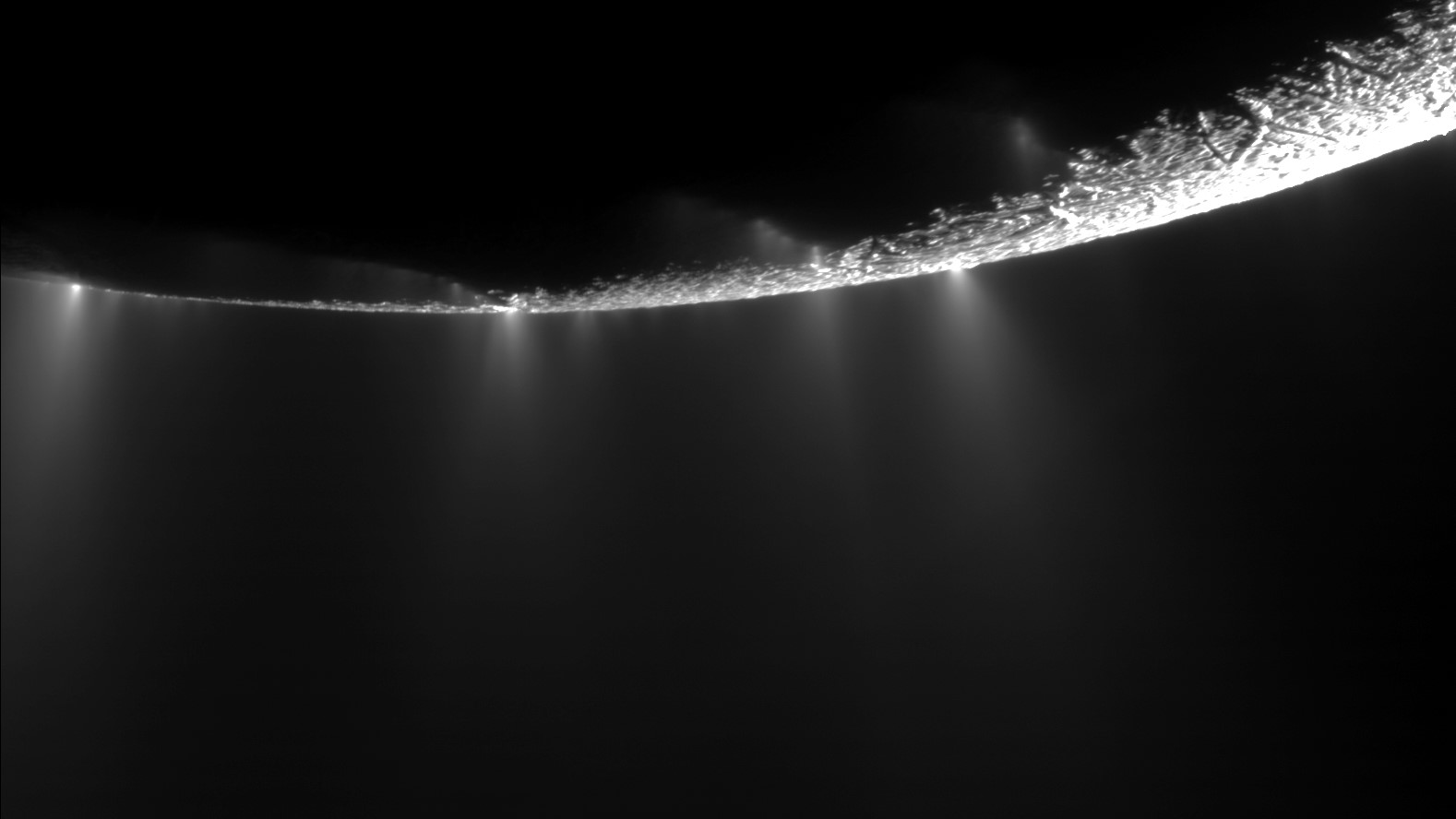 Close up of Enceladus showing water appearing to spray out of the surface into the darkness of space.