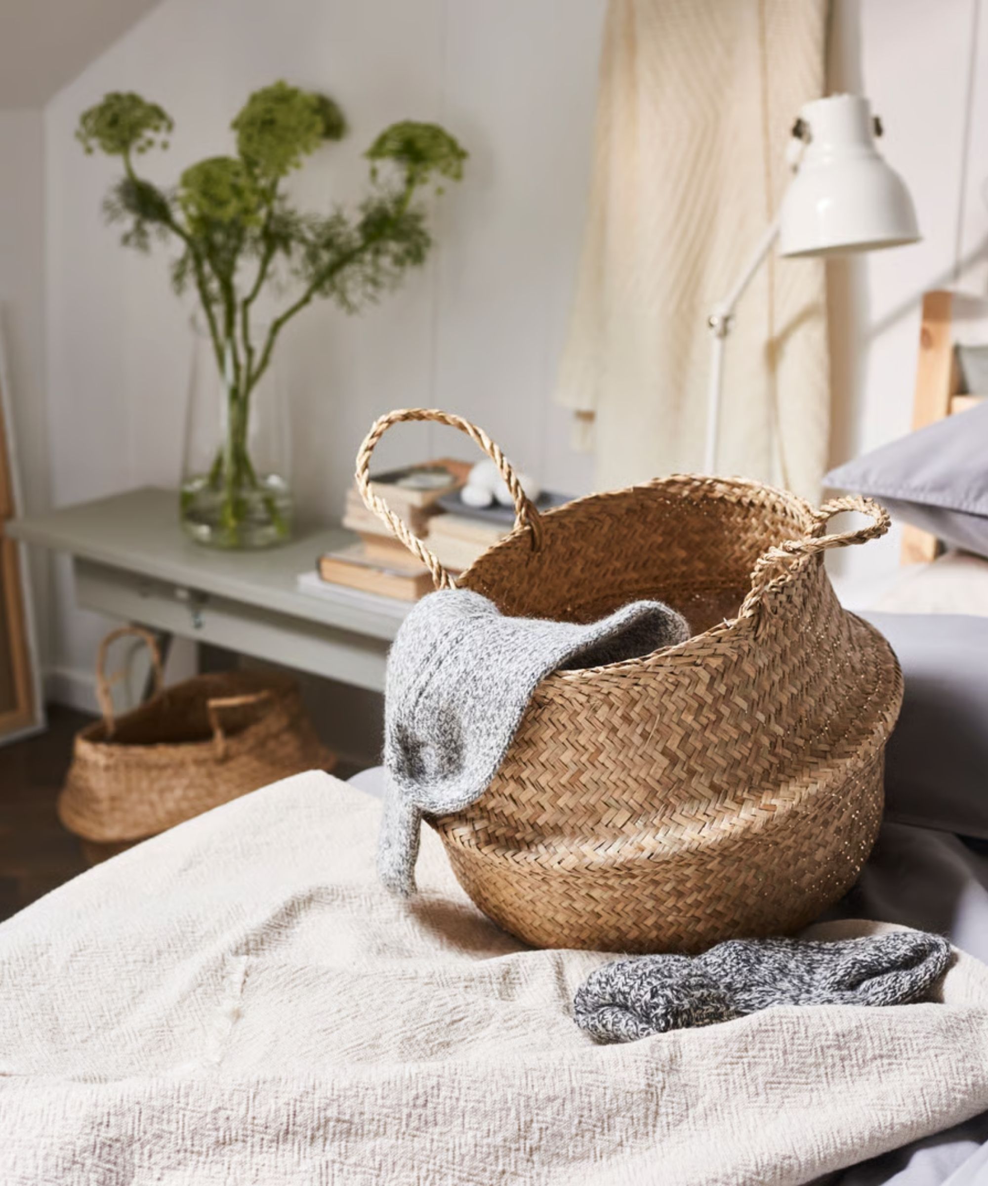 IKEA FL&amp;Aring;DIS Basket pictured on a bed in a neutral bedroom, with a grey side table behind with large green flowers.