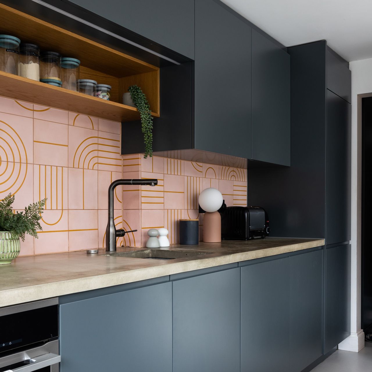 a contemporary dark blue kitchen with pink graphic tiled splashback