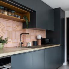 a contemporary dark blue kitchen with pink graphic tiled splashback