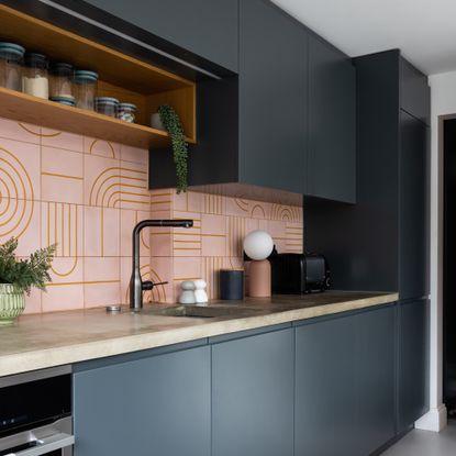 a contemporary dark blue kitchen with pink graphic tiled splashback