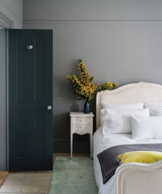 bedroom with gray walls, white bed and vase of flowers on nightstand