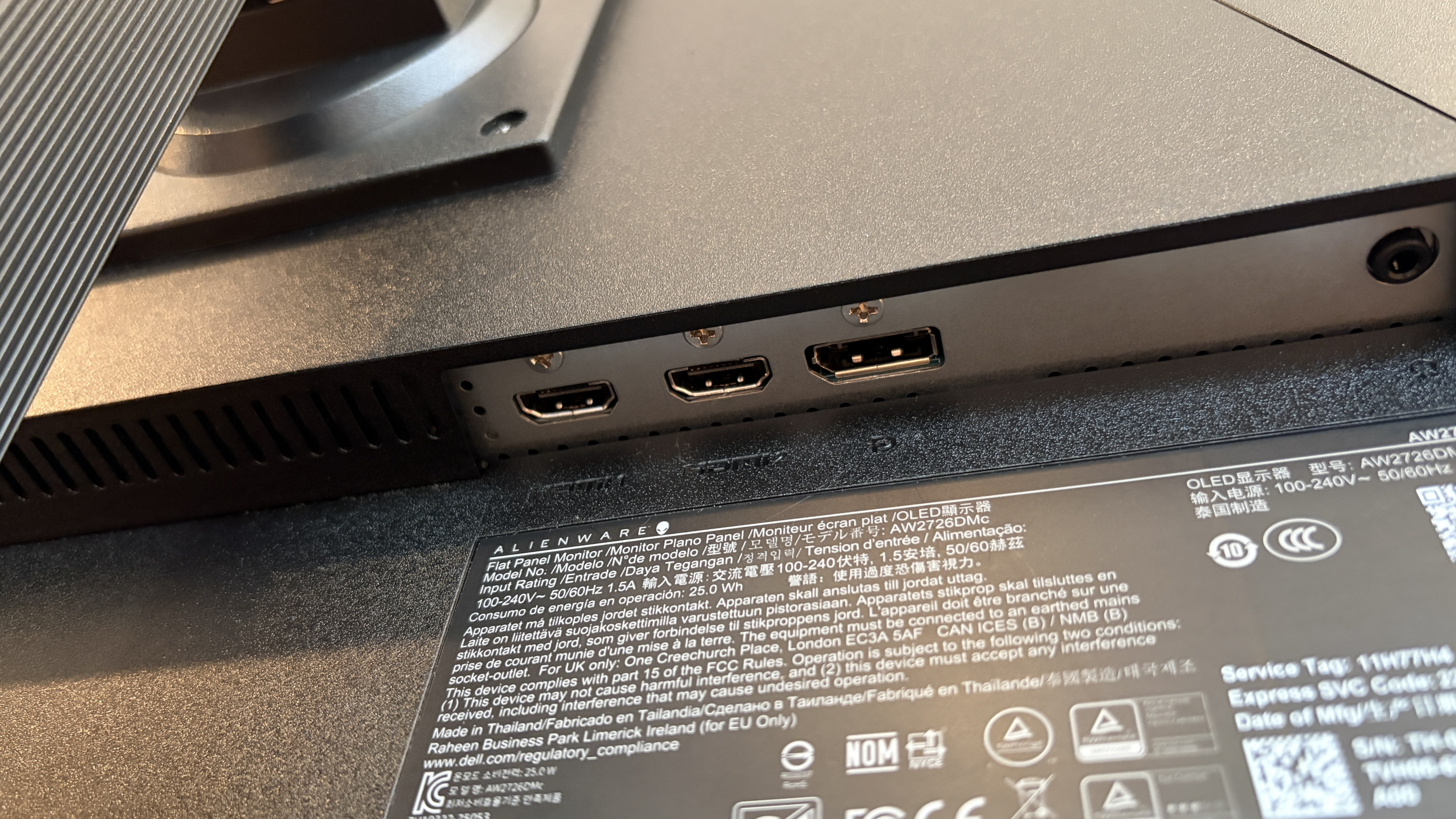 Close-up of a computer monitor's back panel featuring HDMI and DisplayPort inputs. The surface shows brand and safety labels. The lighting is soft and natural.