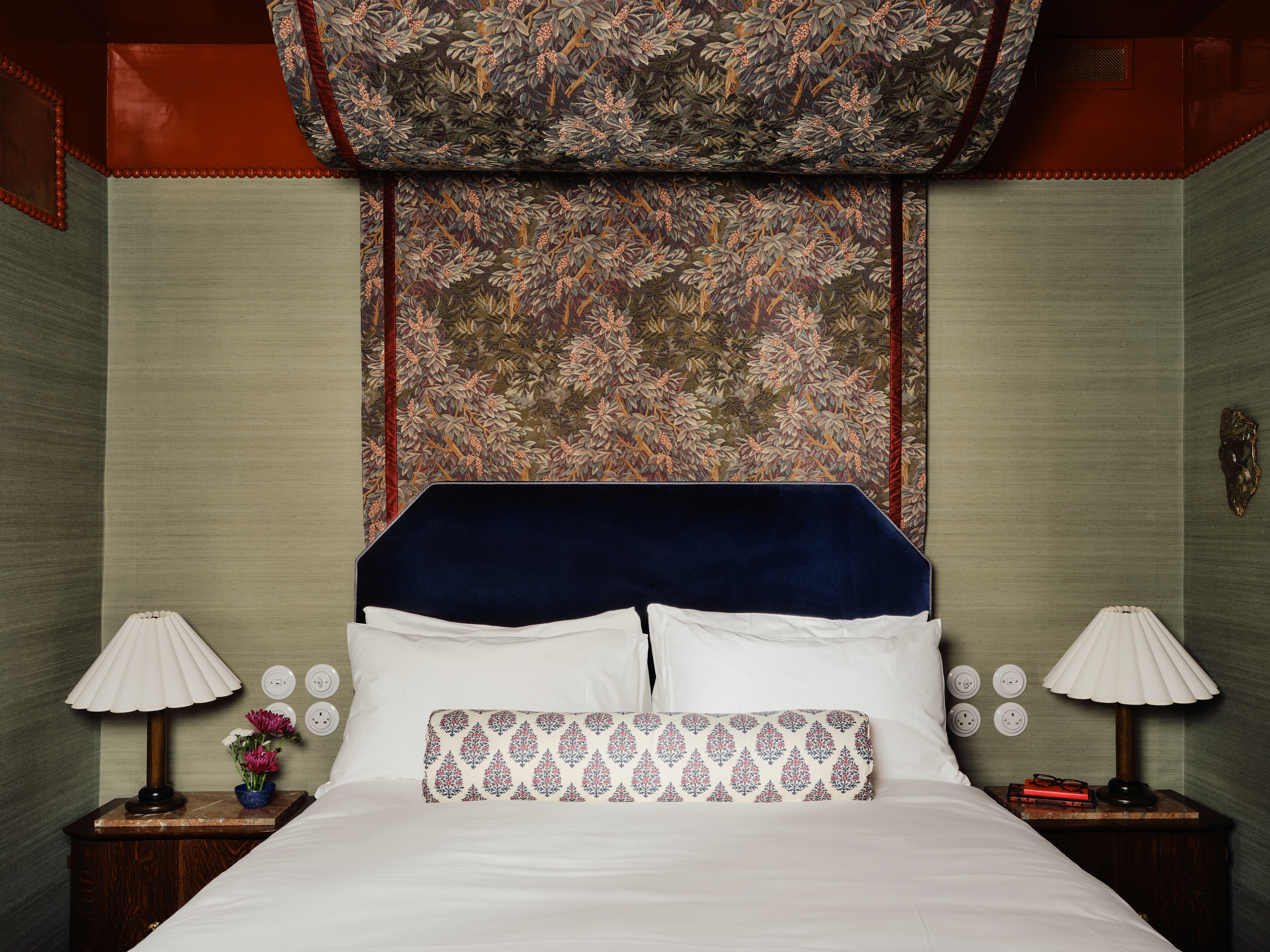 A maximalist hotel room filled with earthy tapestries, dust pink and mint green walls, textural bedside table lamps, eccentric prints and fabrics, and more.