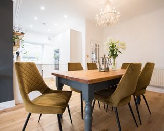 Tidy dining table with all chairs tucked in except for one at an angle, and gleaming glass chandelier above the table