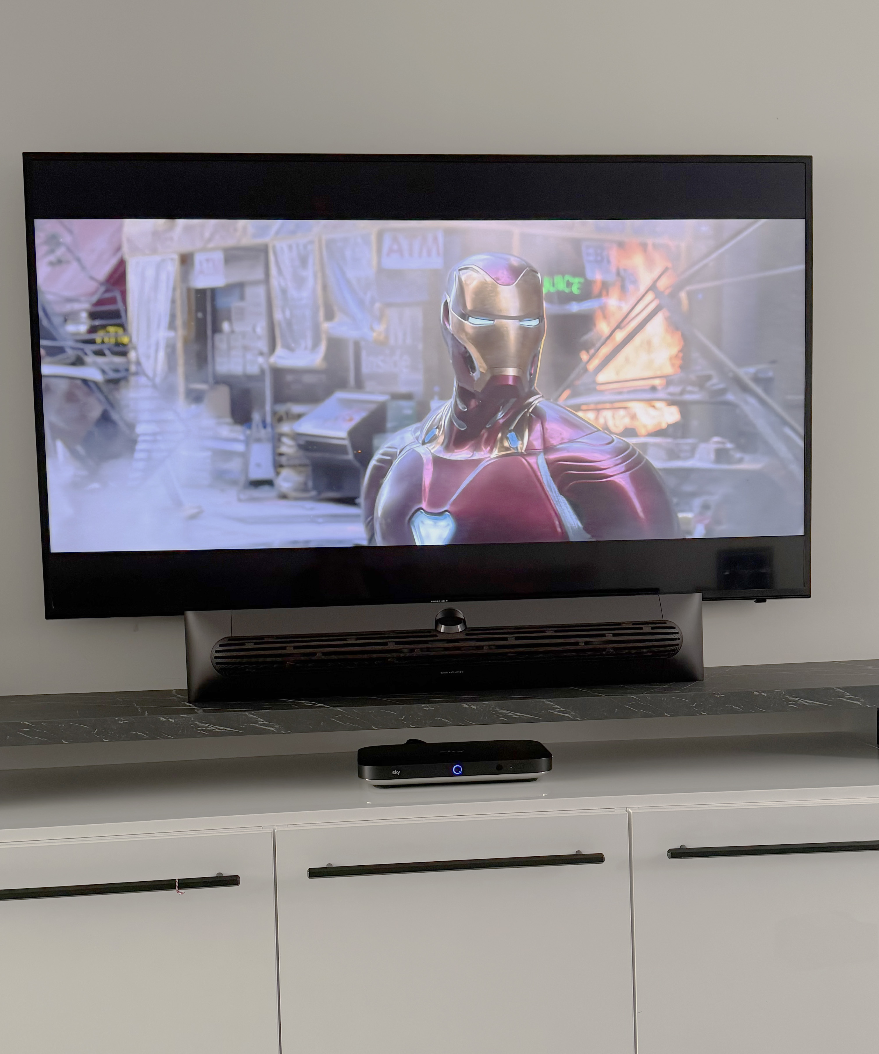 Television displaying a scene from Avengers: Infinity Way showing Iron Man in an action sequence, with the Beosound Premiere soundbar positioned beneath it on a media unit