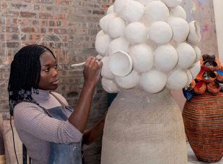 Cape Town-based artist Zizipho Powsa in her studio, working on her Umthwalo series, inspired by the way local women carry heavy loads on their heads. In the background is a finished work titled Umthwalo 4