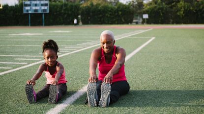 A mom and daughter stretch on a football field.