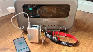 Photo of the Zendure SuperBase Pro 1500w charging a power bank, head lamp and smartphone