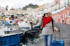 Woman at the harbour with suitcase, talking on mobile phone