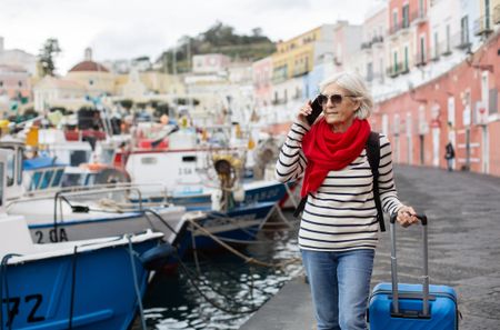 Woman at the harbour with suitcase, talking on mobile phone