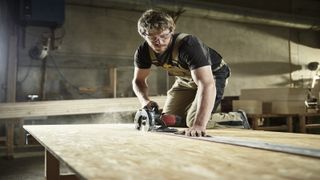 Man in safety goggles cutting timber with circular saw uses