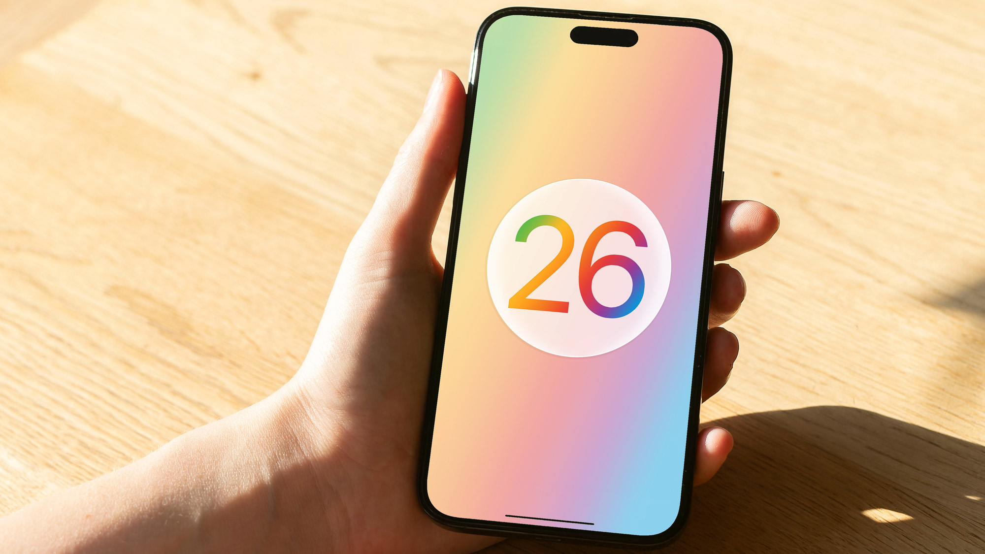 A render of the Apple iOS 26 logo on an iPhone held in a hand.