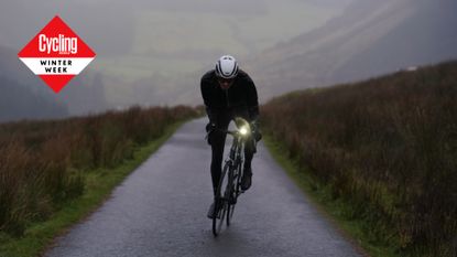 Man riding a bike in winter kit with light on small road in Wales