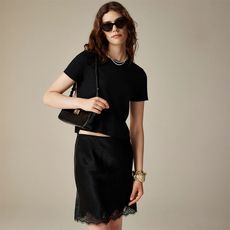 model wears black tee and black skirt with lace trim and carries a black handbag with sunglasses and pearl necklaces