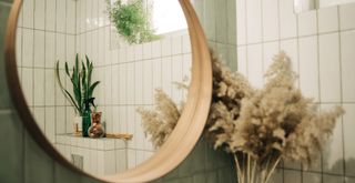 white tiled bathroom with wooden oval mirror shown from the side to show an important step of how to clean a mirror by checking all angles