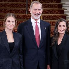Queen Letizia, Princess Leonor and King Felipe smiling in suits in front of a staircase