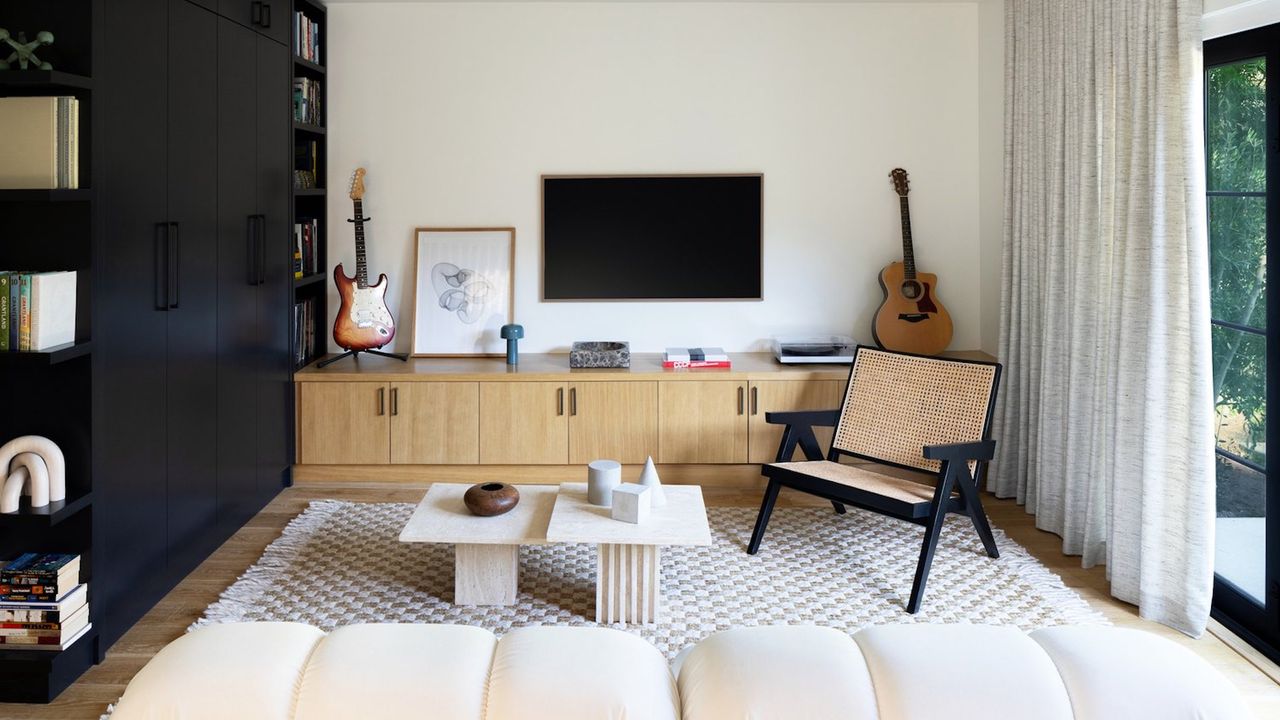 Living room with large neutral rug, sofa, armchair and storage furniture with white walls and wood floor