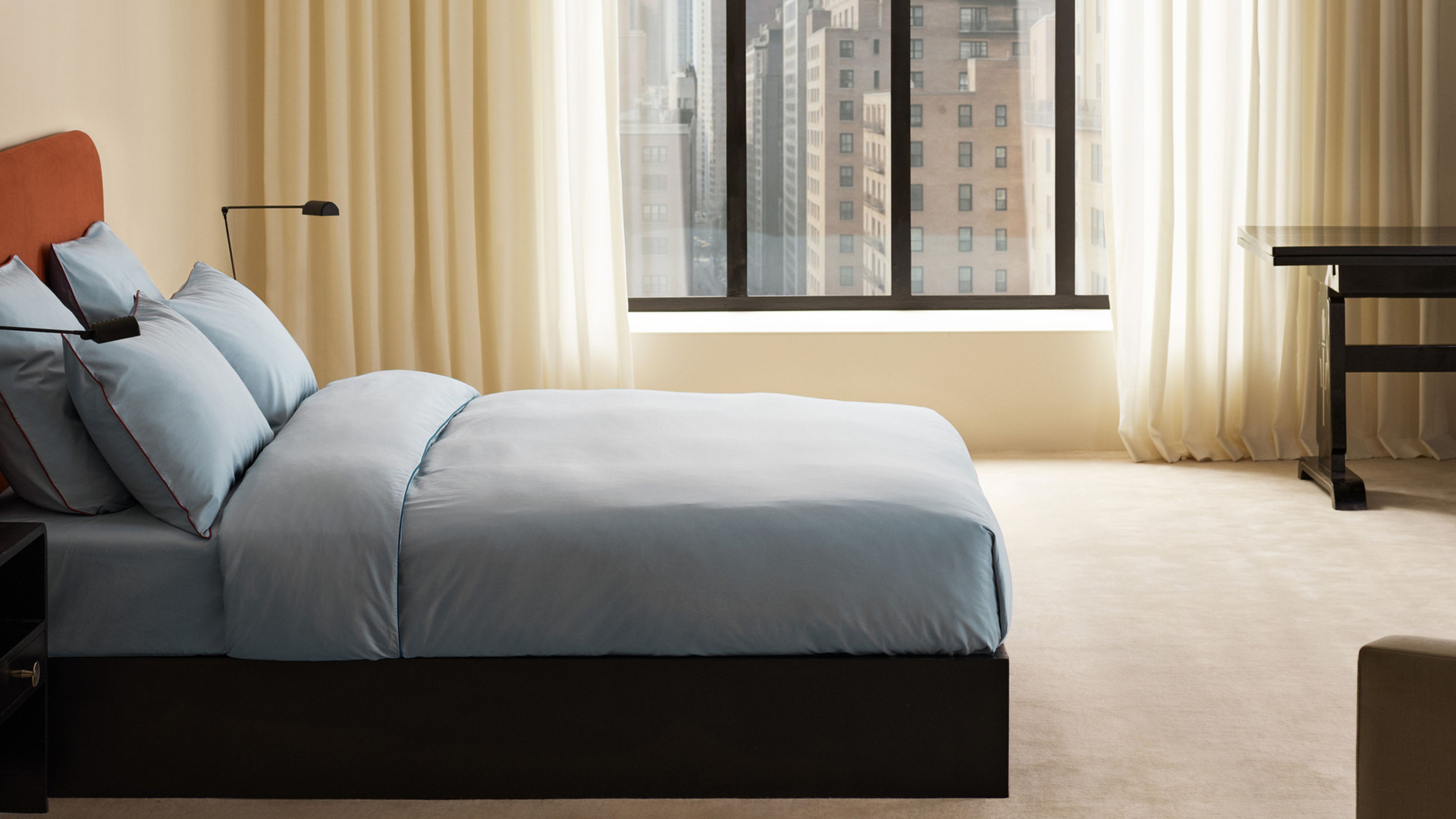 Minimalist NYC bedroom styled with a cream-colored wool rug, matching sheet curtains, and an 'ice blue' bedding set by Nordic Knots