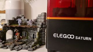 Elegoo Saturn printer alongside 3D-printed ruins and fantasy miniatures