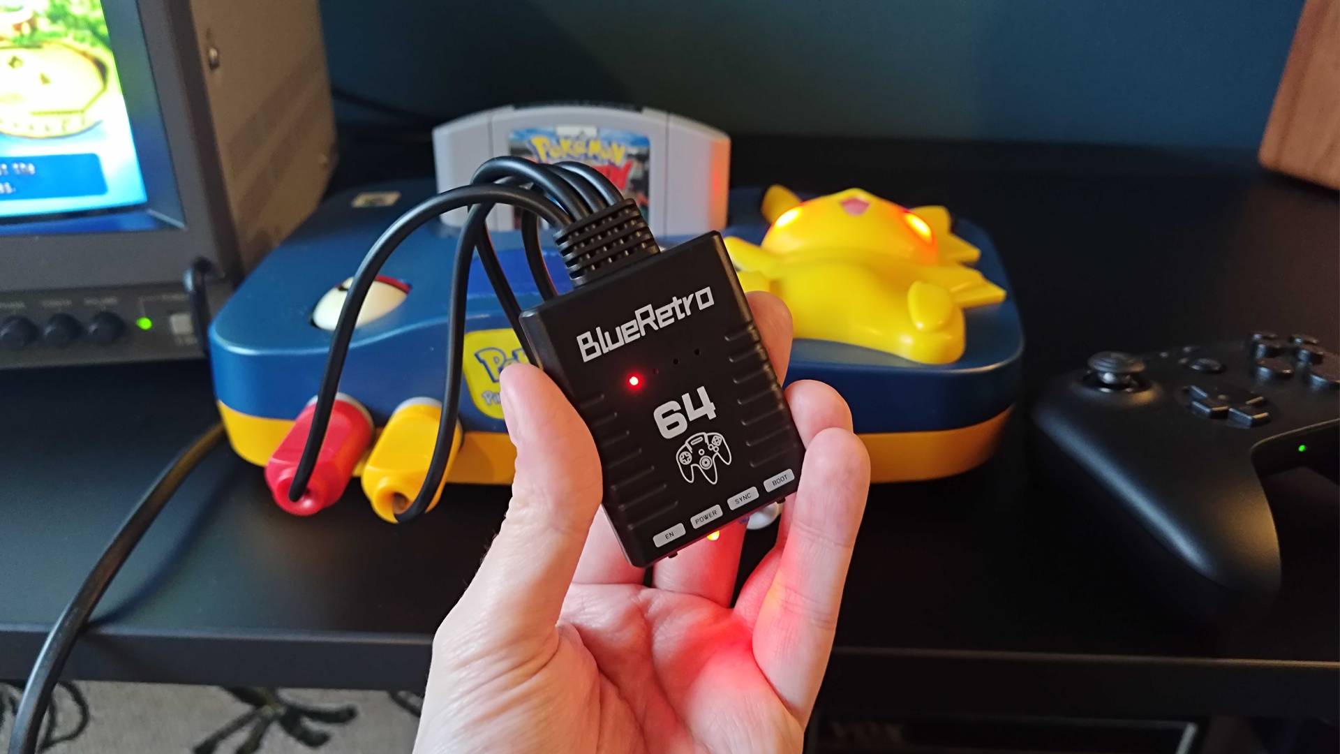 Hand holding Blueretro N64 controller adapter in front of Pikachu N64.
