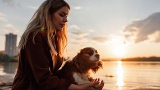 Woman holding dog’s paw at sunset