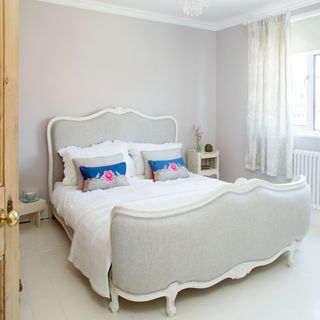 King sized bed with ornamental grey headboard and matching footboard with white trim. Complete with blue patterned cushions