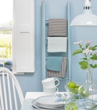 Blue painted towel ladder for tea towels on blue wall in kitchen next to white table and window