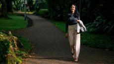 Woman walking down park pathway on sunny day holding jacket in hand