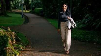 Woman walking down park pathway on sunny day holding jacket in hand