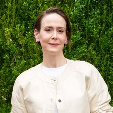 a white woman with short hair wearing a cream sweater and posing in front of a grass wall