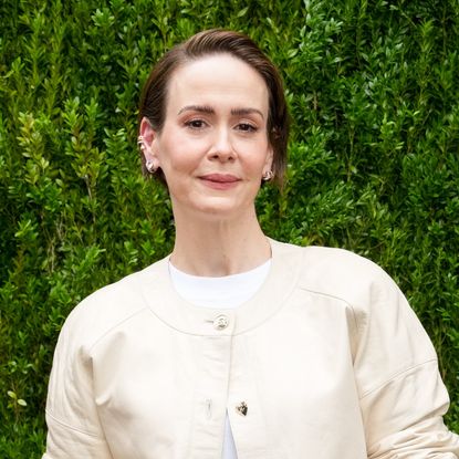 a white woman with short hair wearing a cream sweater and posing in front of a grass wall