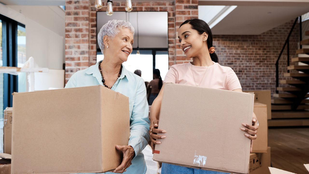 A mother and daughter smile at each other while holding moving boxes.