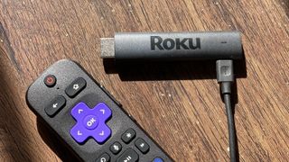 A Roku firestick and a TV remote on a wood-finish desk