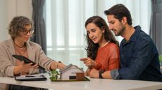 A financial expert sits in front of a house model and assists a couple in navigating their home sale