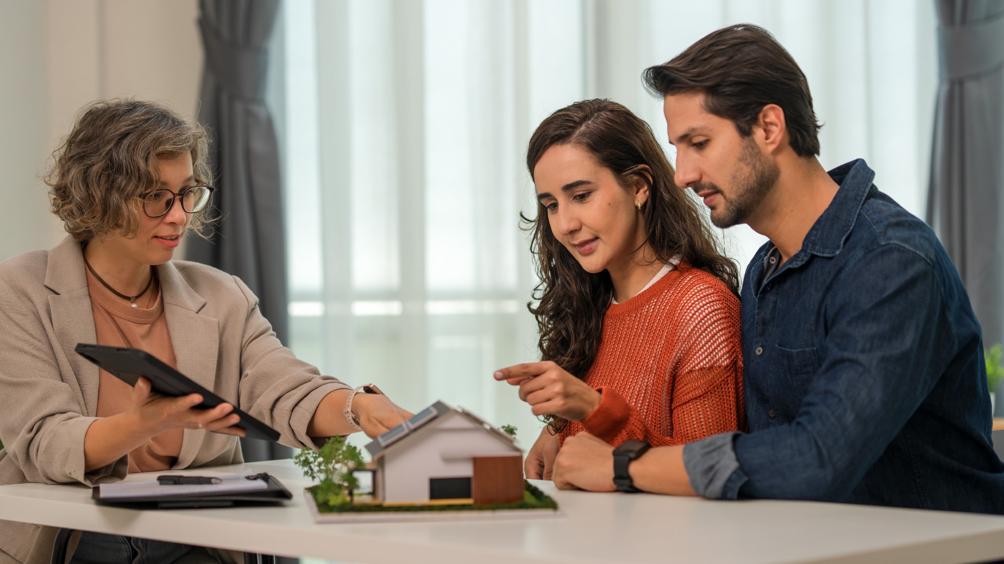 A financial expert sits in front of a house model and assists a couple in navigating their home sale