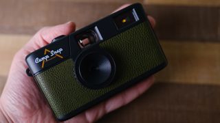 The Camp Snap camera, in forest green, sits in a person's hand