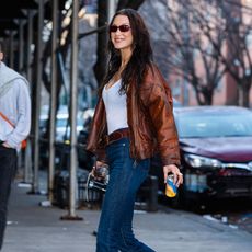 Bella Hadid wears brown bomber jacket, white tank top, dark wash jeans and a brown pair of adidas SL 72