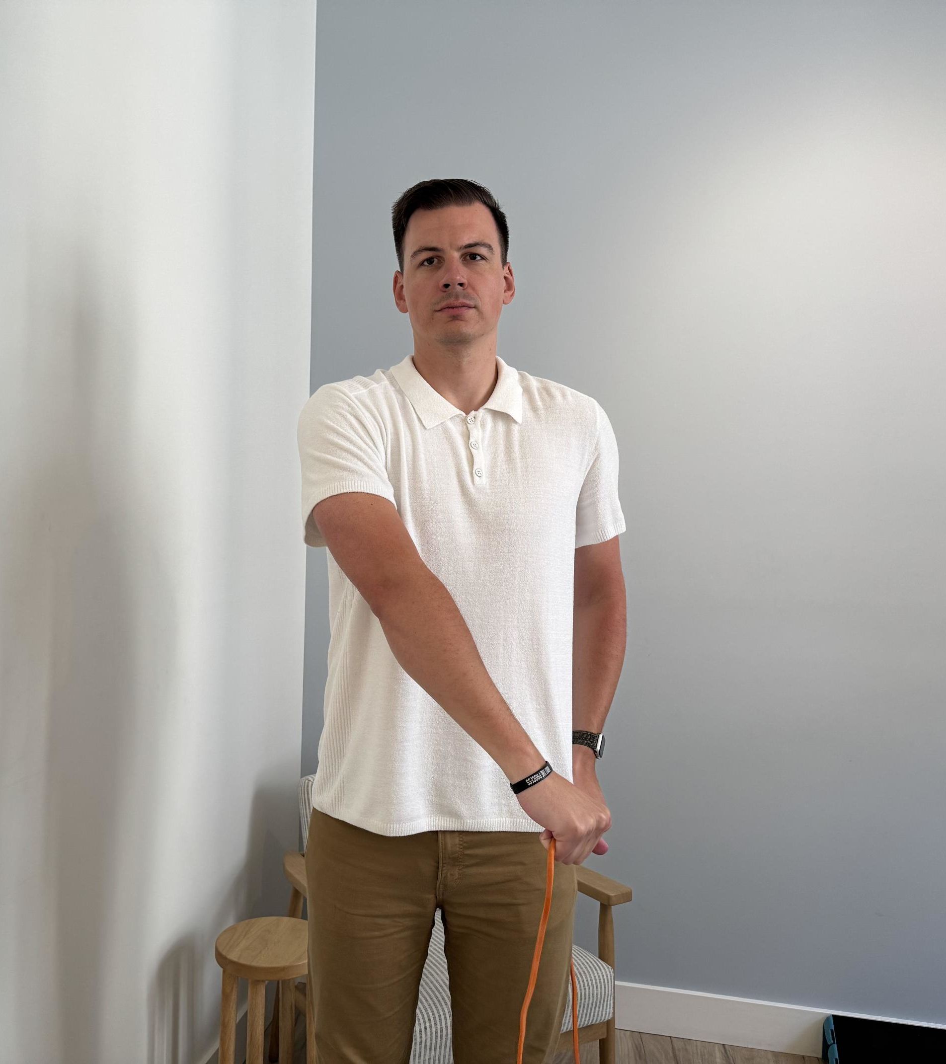 A man holding a thin orange resistance band by his left hip