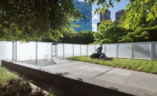 white garden fencing around a lawn with a statue of a lady , tall buildings can be seen in the distance