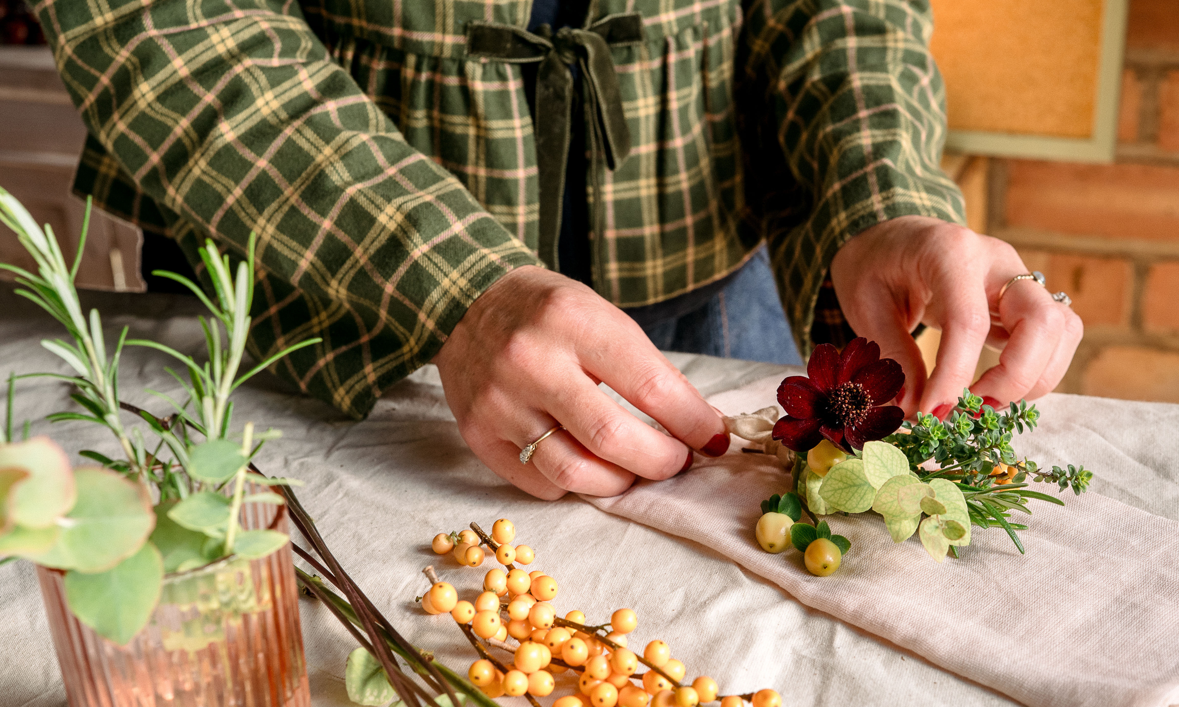 Hands arranging flowers and foliage on a pink cotton napkin