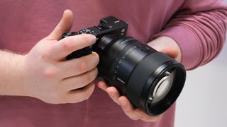 Sony FE 135mm lens attached to a sony camera and held in a pair of hands