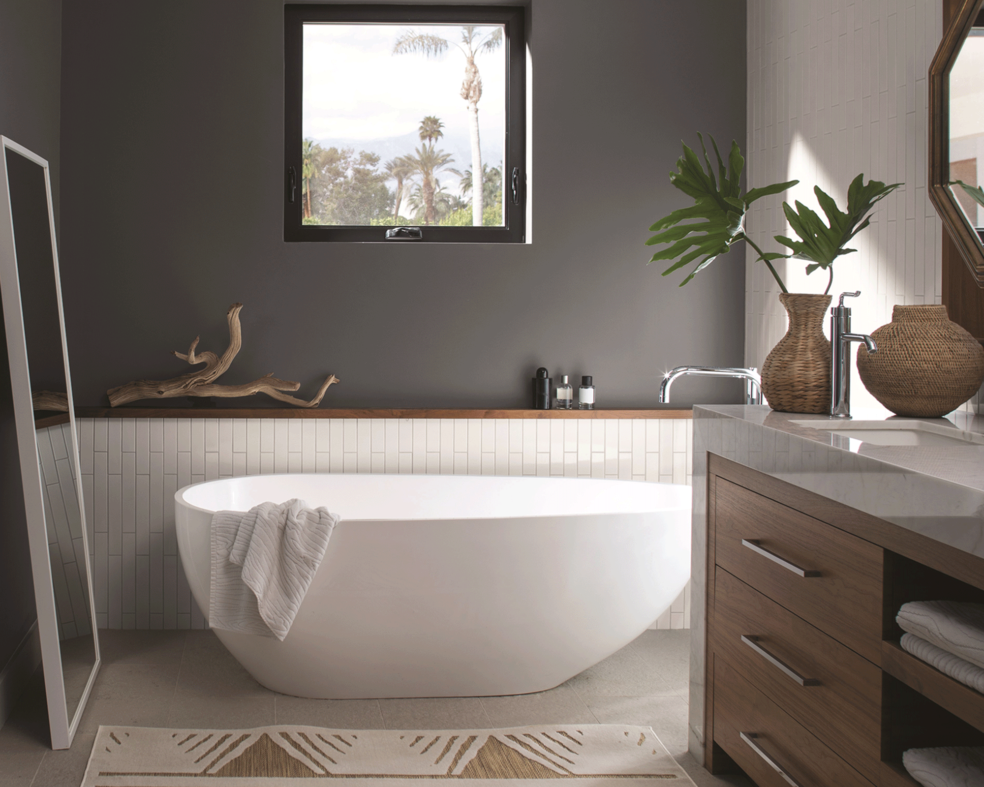 A small white bathtub in bathroom with white metro tiling, dark grey wall decor and wooden vanity
