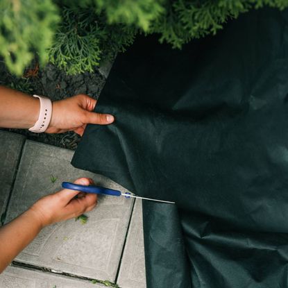 Hands using scissors to cut landscape fabric