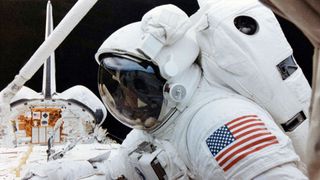 A black man in a white spacesuit works in the payload bay of the space shuttle