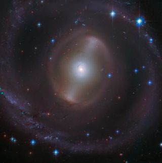 a bright central point radiates outward with swirling arms of subtle gas and a scattering of bright blue points of light in the black of space.